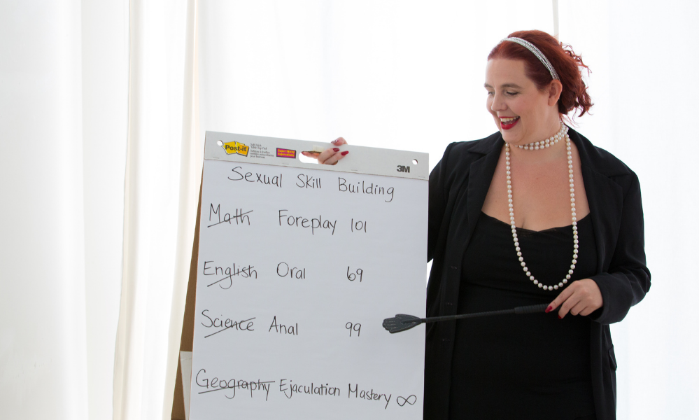 Gaia Morrissette is holding a riding crop, while pointing at white board. She is teaching a class