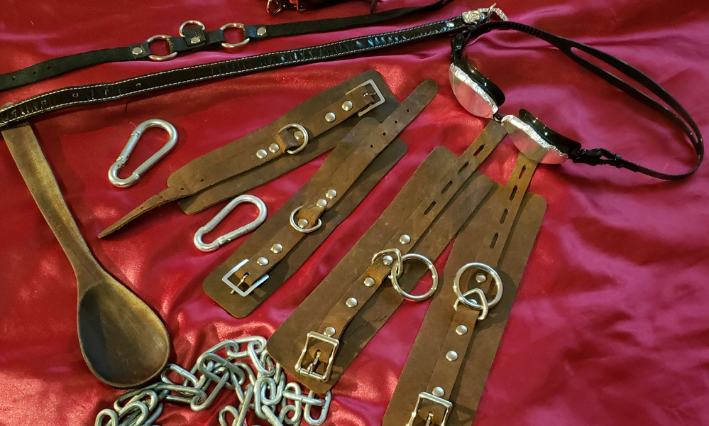 Many BDSM tools- chains, leather cuffs, collar,wooden spoon, goggles